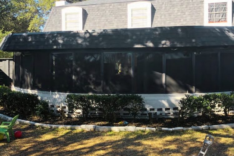 Backyard screened porch, landscaped with shrubs and stone border.