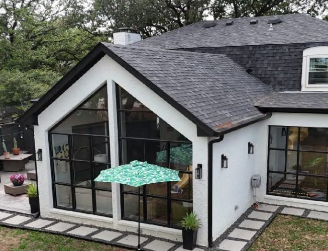 Modern home with black roof, white exterior, and a glass sunroom addition overlooking a patio.